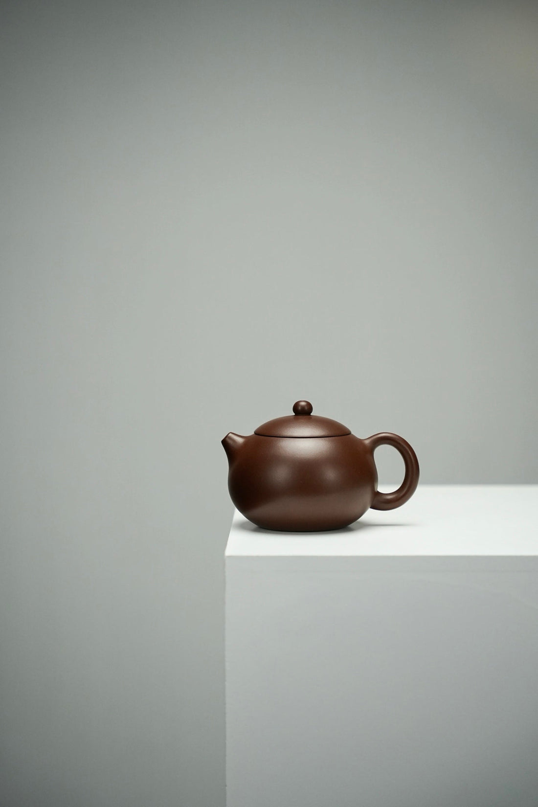 Side view of a brown Xi Shi teapot with a rounded body, short spout and loop handle