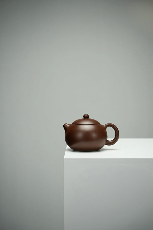 Side view of a brown Xi Shi teapot with a rounded body, short spout and loop handle