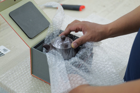 A wrapped teapot being placed in a box with bubble cushioning