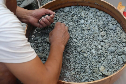 Hands sorting small pieces of raw clay material in a round tray