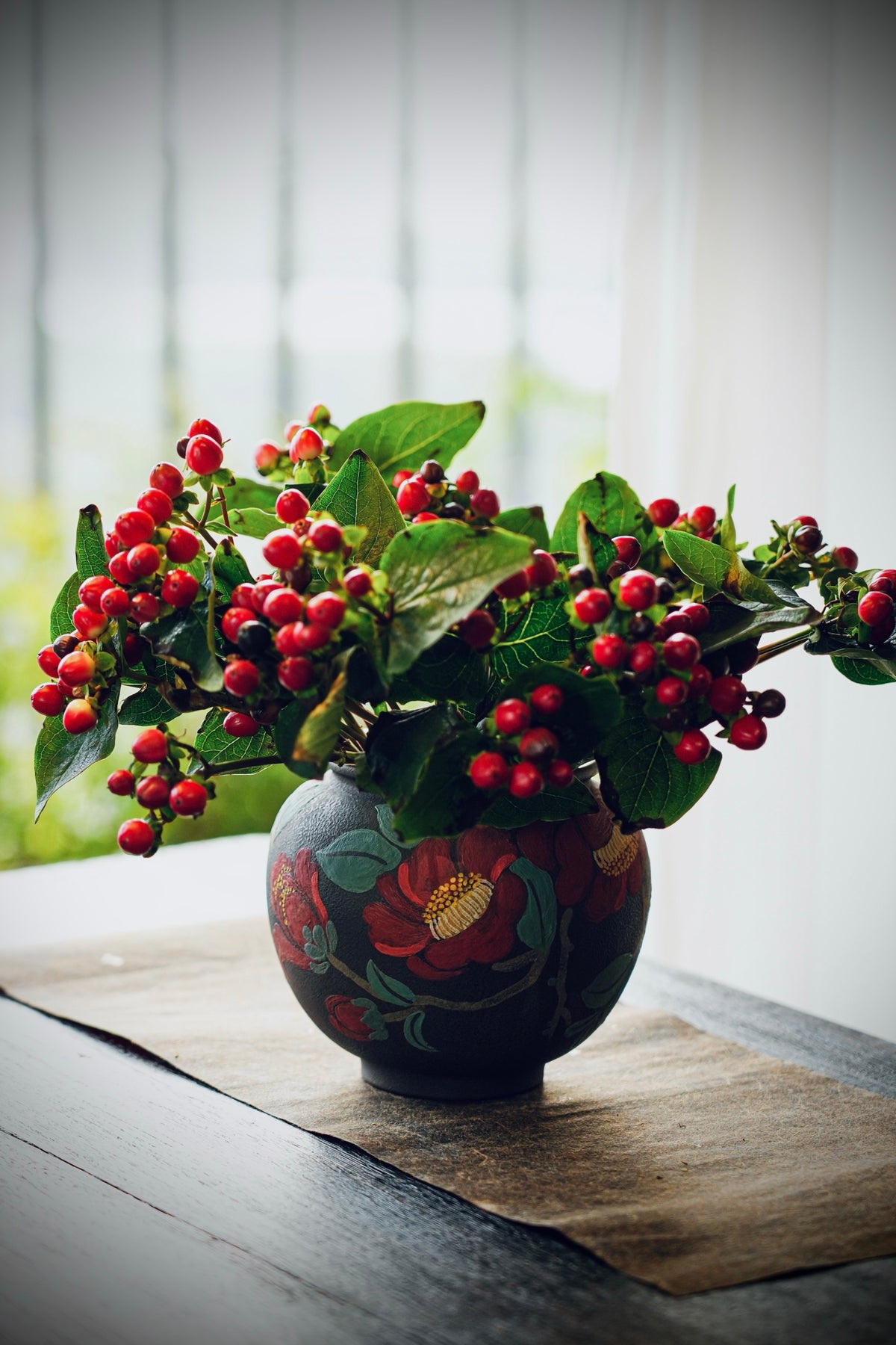 Red floral vase styled with leafy berry stems